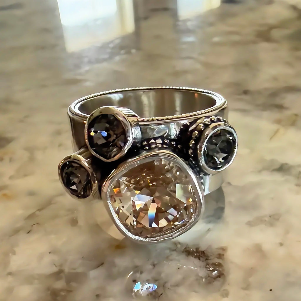 A silver-toned statement ring with a wide band, featuring a large cushion cut Swarovski crystal and three smaller round smoky crystals.